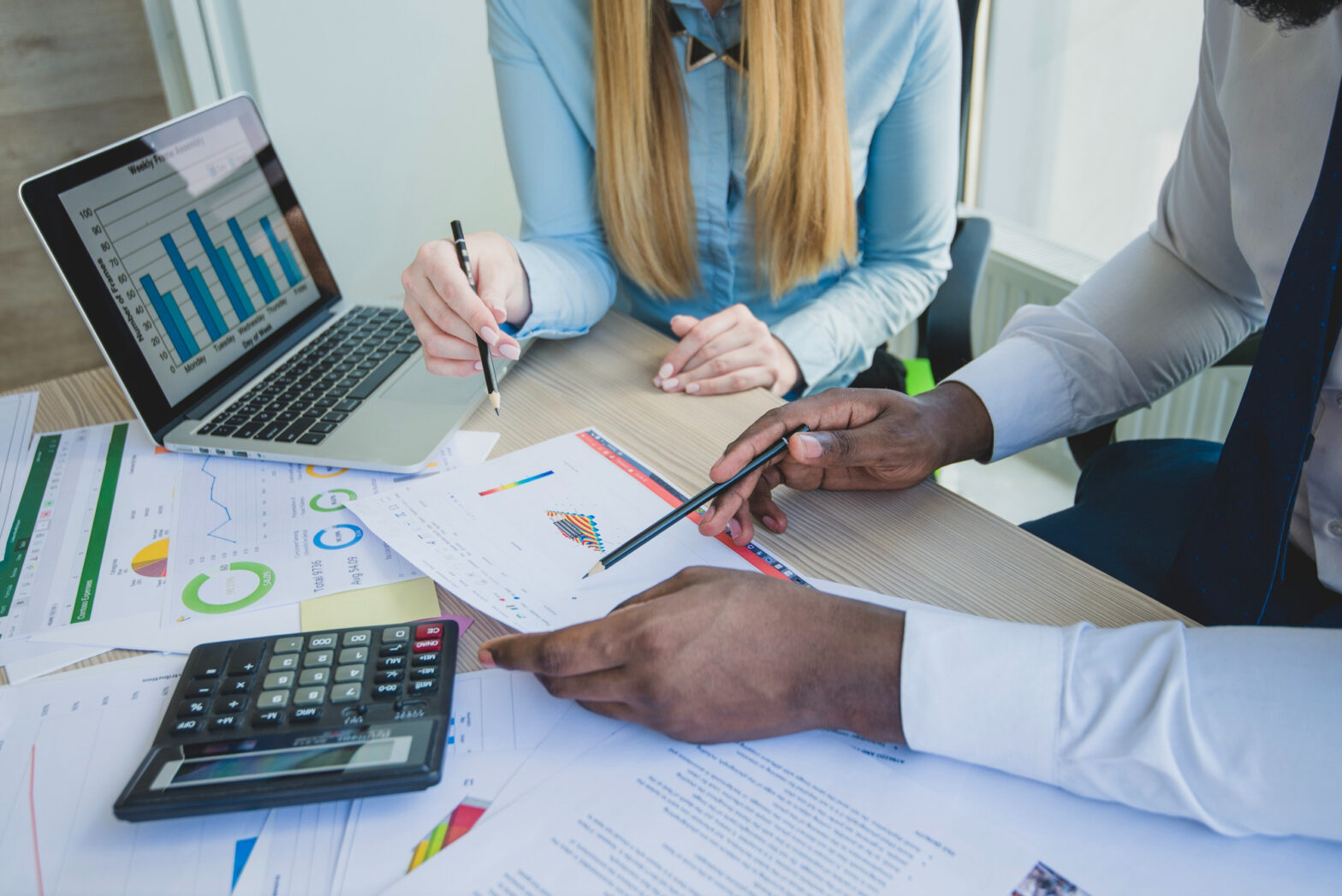 A business owner analyzing financial documents with a calculator and laptop, symbolizing effective management of business finances.